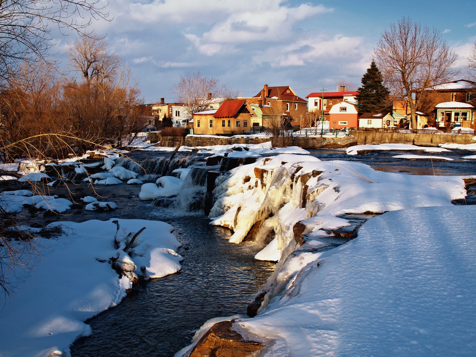 Les chutes de la rivière Saint-Louis en hiver, avec les maisons du vieux Beauharnois derrière