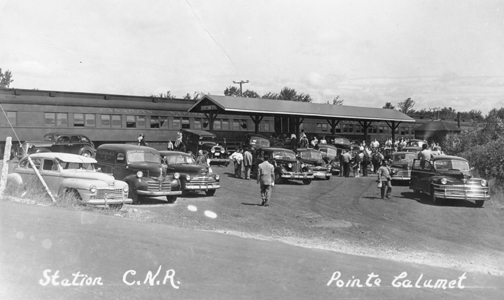 La gare du Canadien National à Pointe-Calumet vers 1950, avec des voitures d'époque et des vacanciers