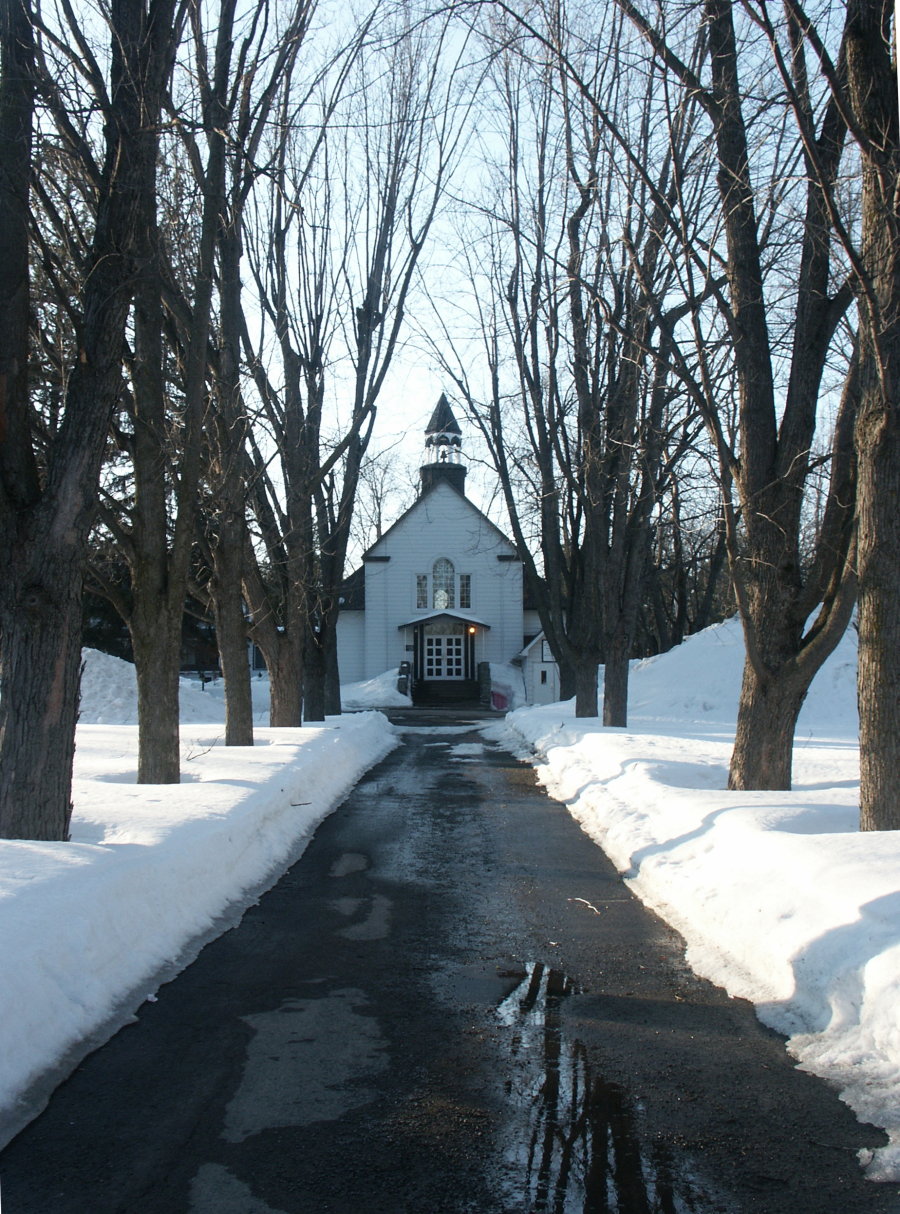 Petite église blanche au bout d'une allée bordée de grands arbres, à Rosemère