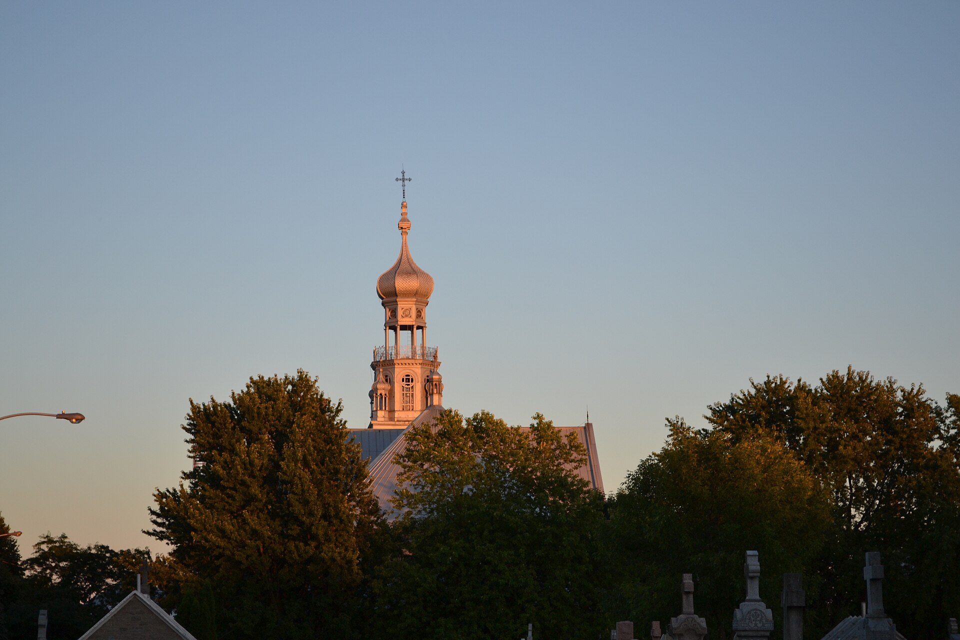 Le clocher à bulbe de l'église de Sainte-Anne-des-Plaines au-dessus des arbres, au coucher du soleil